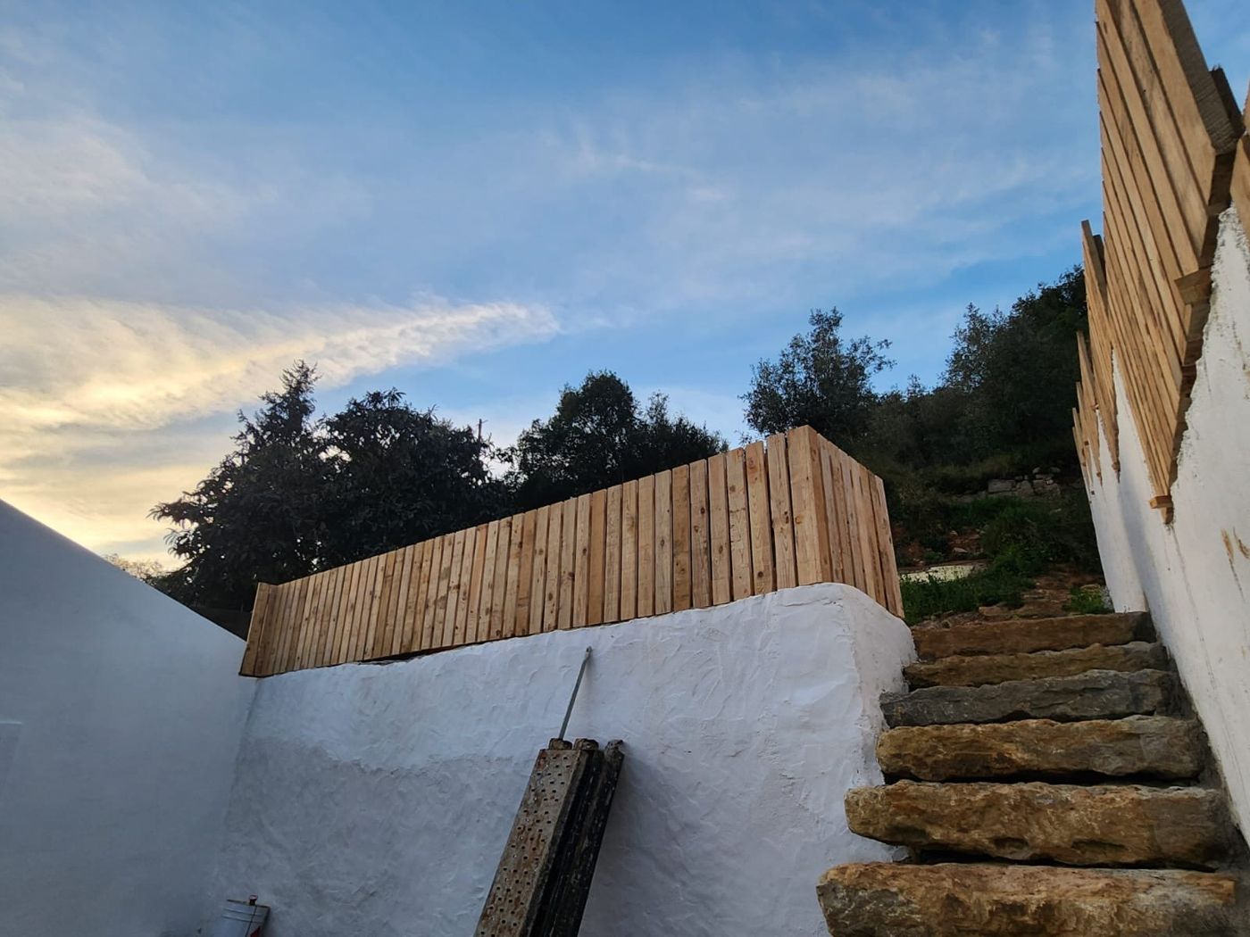 Escadaria em pedra acabada, com muro branco e vedação em madeira